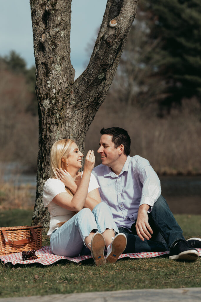 bride looks into grooms eyes. they are sitting on a picnic blanket sharing food and smiling.