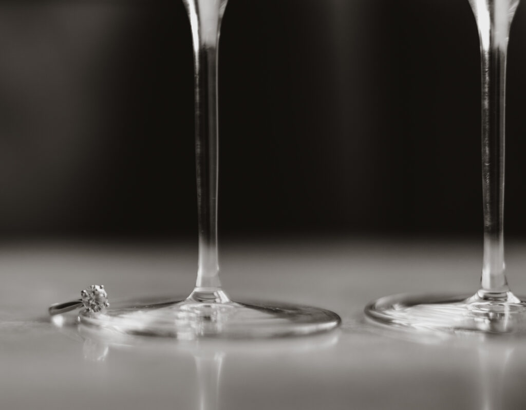 modern moody black and white photo of ring and wine glasses